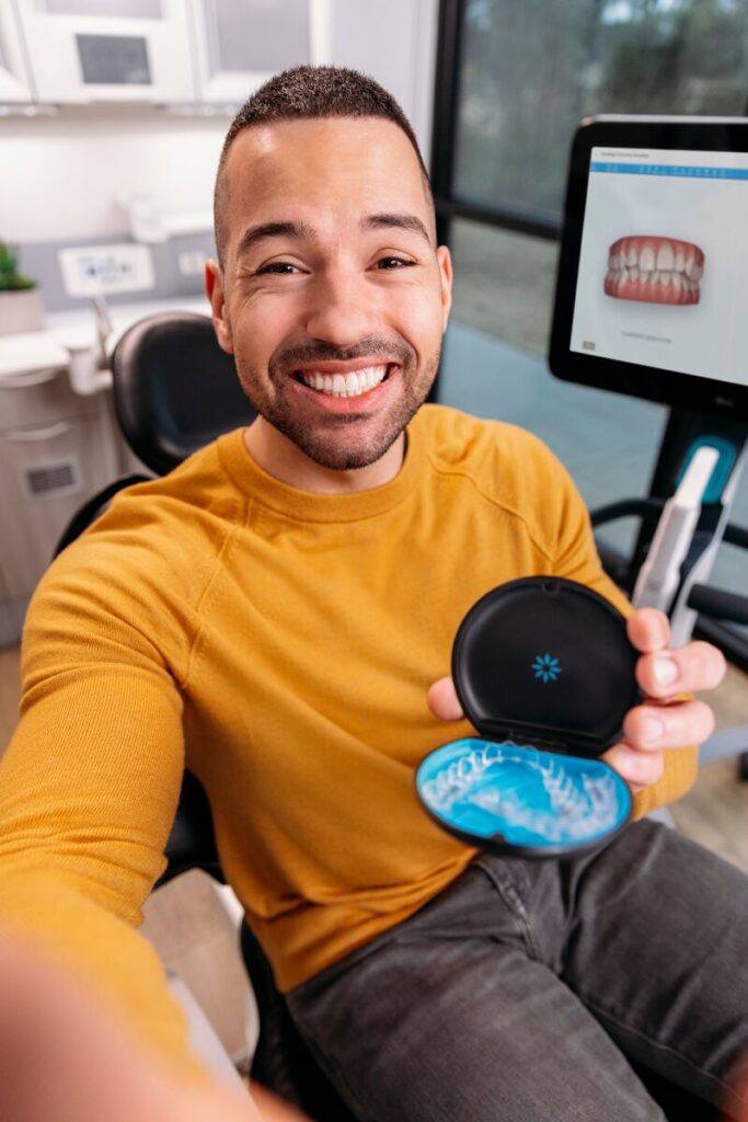 Smiling patient holding an Invisalign clear aligner